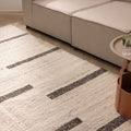 Handwoven white and brown wool-blend flatweave rug with a modern striped pattern in a living room setting.