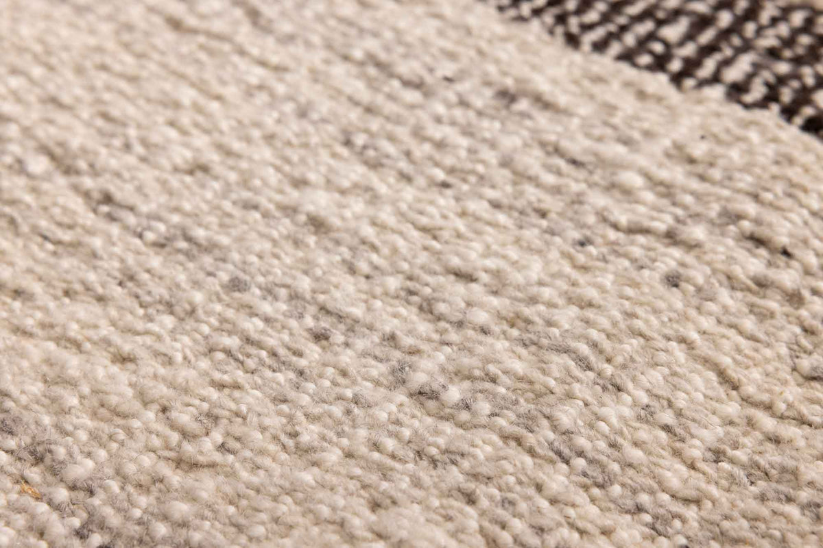 Close-up of a handwoven white and brown wool-blend flatweave rug with a textured, durable kilim design.