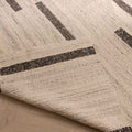 Handwoven white and brown wool-blend flatweave rug with a modern geometric stripe pattern and a folded corner.