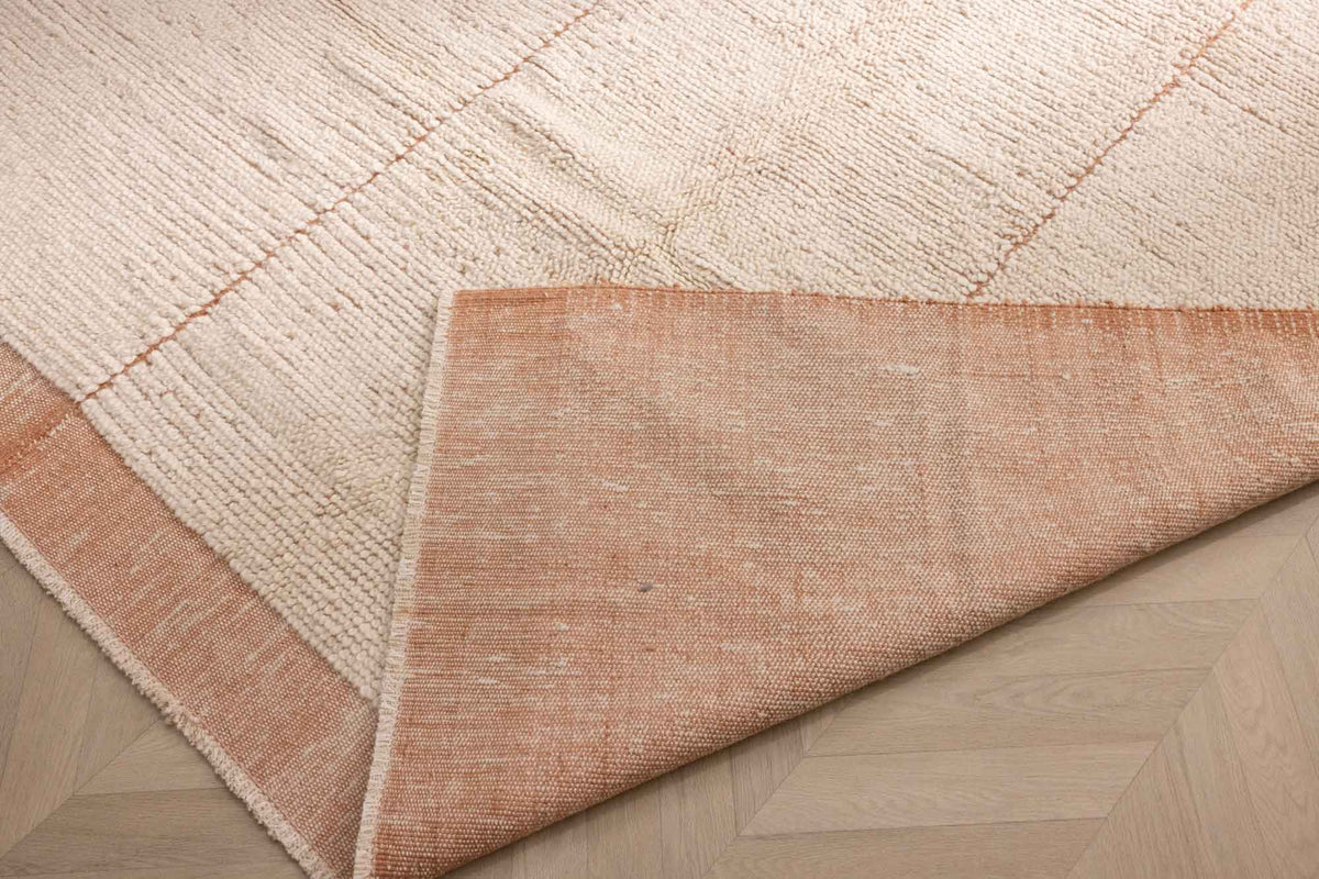 Handwoven apricot shaggy wool rug with a thick pile, grid pattern, and folded corner showing the durable cotton backing.