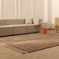 Beige sectional sofa in a living room with a brown rug and wooden cabinet.