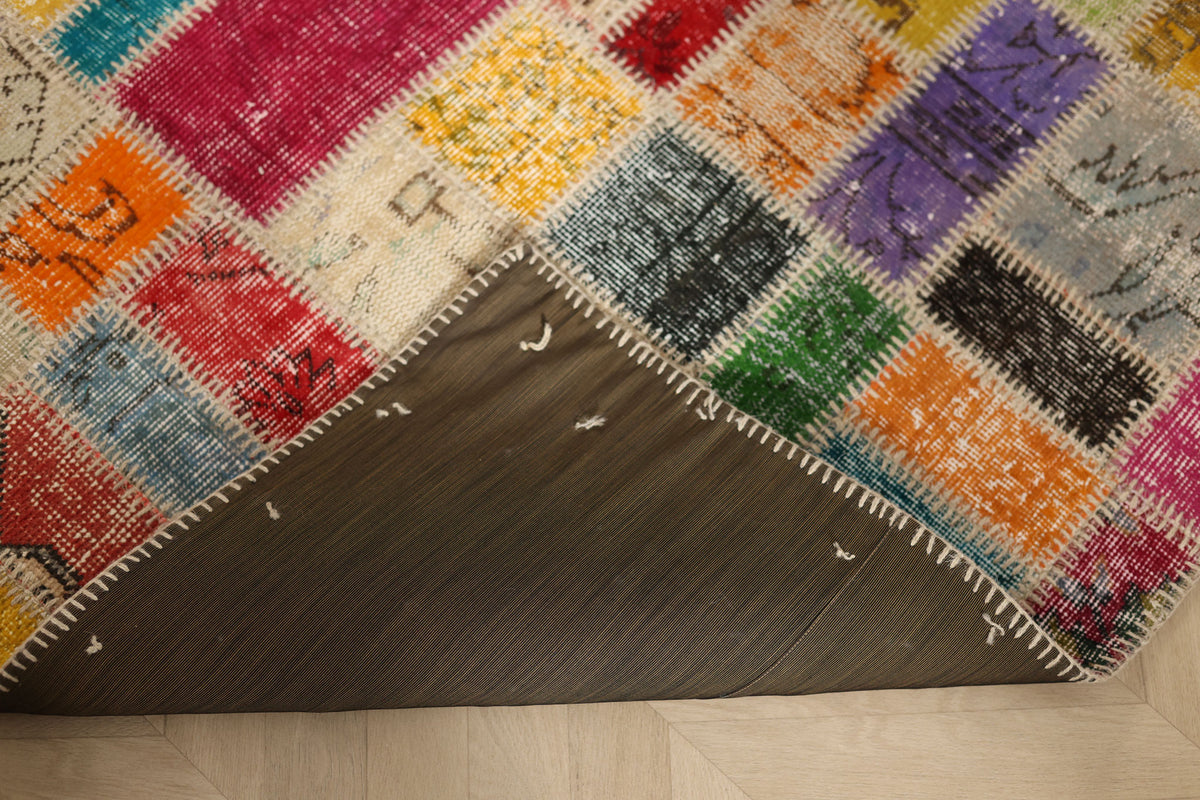 Handmade 5x8 ft patchwork Turkish rug with vibrant floral wool and cotton squares and a stitched dark fabric backing.