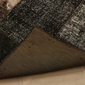 Handmade black patchwork Turkish area rug with distressed wool and cotton textures and a folded corner showing the backing.