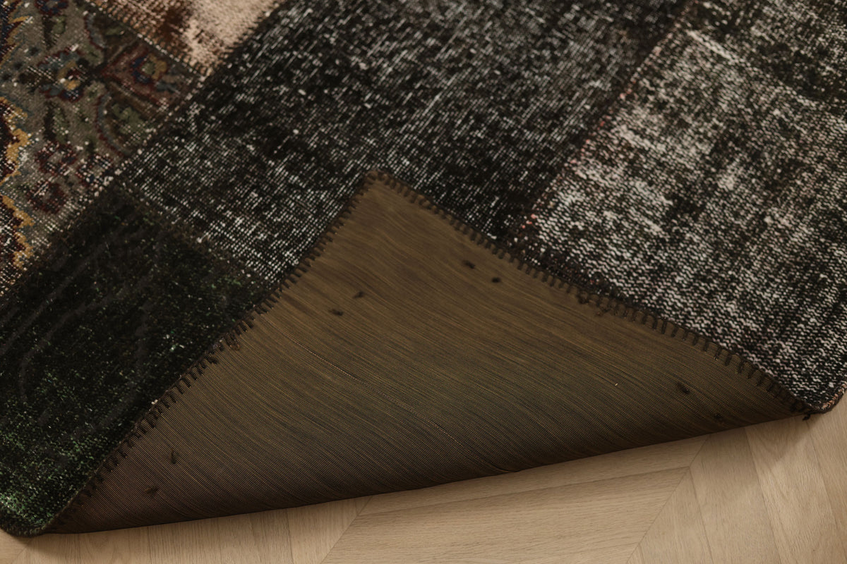 Handmade black patchwork Turkish area rug with distressed wool and cotton textures and a folded corner showing the backing.