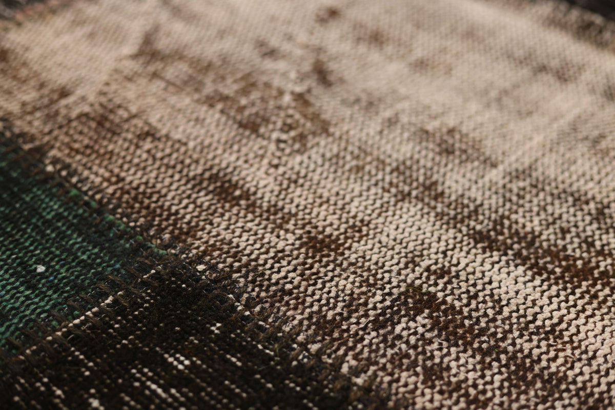 Close-up of a black and brown distressed patchwork wool and cotton vintage Turkish rug with textured weave.