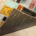 Handmade 5x8 ft vintage Turkish patchwork rug with colorful floral wool and cotton patterns and a dark fabric backing.