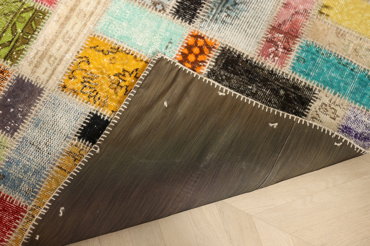 Handmade 5x8 ft vintage Turkish patchwork rug with colorful floral wool and cotton patterns and a dark fabric backing.