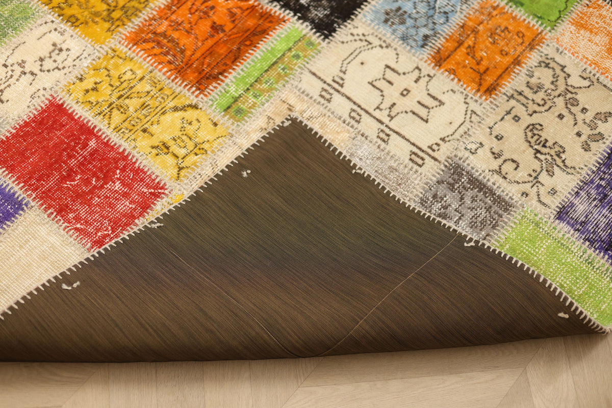 Handmade 5x8 ft vintage Turkish patchwork rug with vibrant floral wool and cotton squares and a dark protective backing.