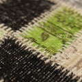Close-up of a handmade Turkish patchwork rug featuring stitched wool and cotton squares in vibrant green, black, and neutral tones.