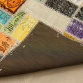 Handmade 5x7 ft vintage Turkish patchwork rug with vibrant floral patterns, wool and cotton blend, showing a dark fabric backing.