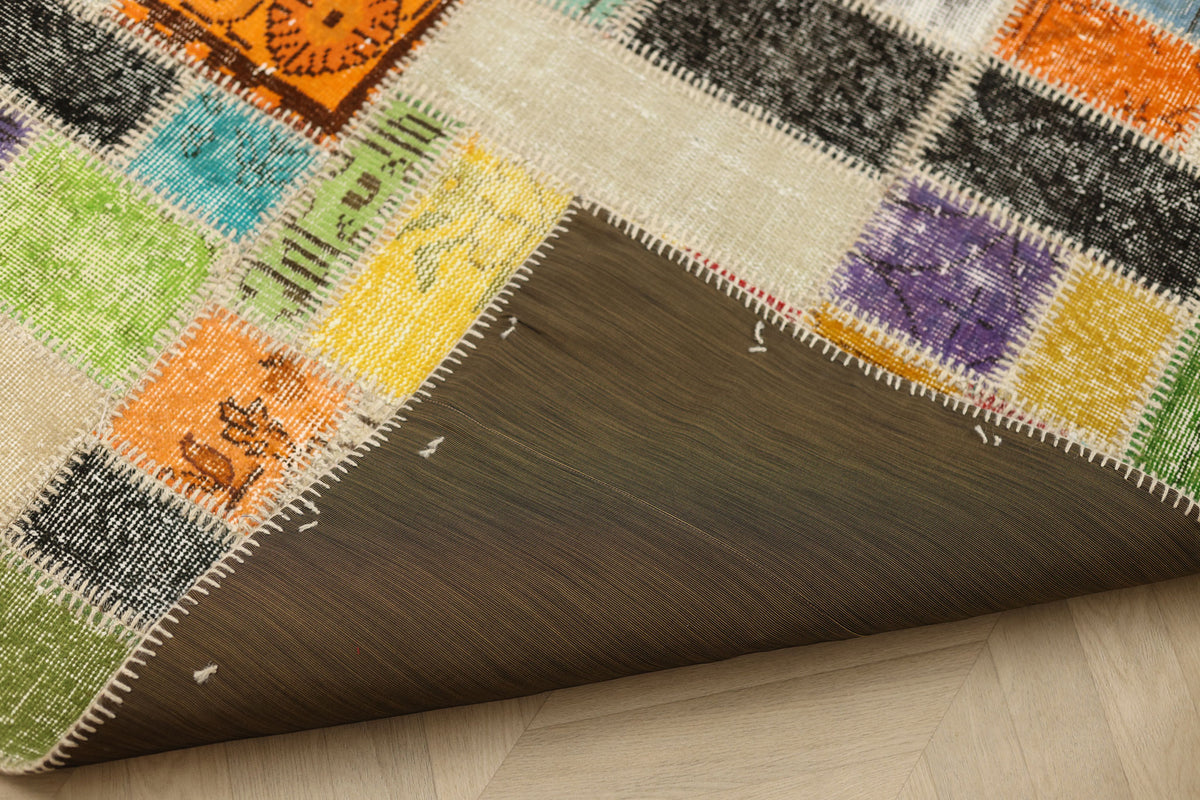 Handmade 5x7 ft vintage Turkish patchwork rug with vibrant floral patterns, wool and cotton blend, showing a dark fabric backing.
