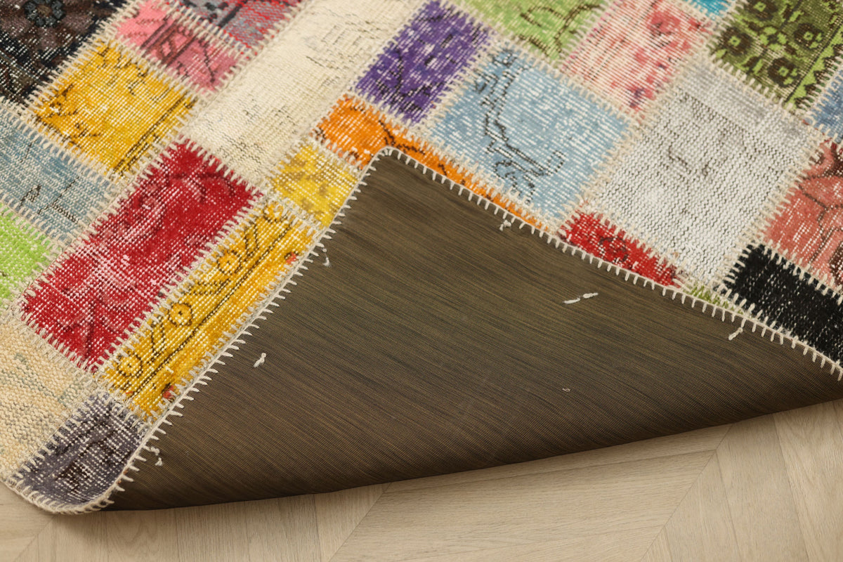 Handmade 5x7 patchwork Turkish rug with vibrant geometric wool and cotton squares and a dark fabric backing.