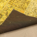 Vintage yellow patchwork Turkish area rug with a dark brown fabric backing and hand-stitched details on a wooden floor.