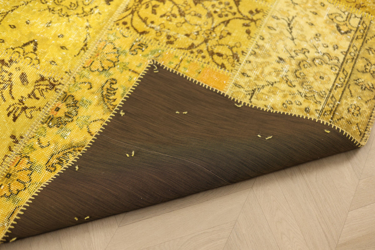 Vintage yellow patchwork Turkish area rug with a dark brown fabric backing and hand-stitched details on a wooden floor.