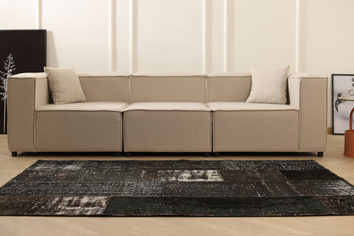 Handmade black patchwork wool and cotton area rug with distressed vintage patterns in a modern living room.