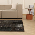 Vintage black patchwork Turkish area rug in wool and cotton with a distressed, overdyed bohemian design on a wooden floor.