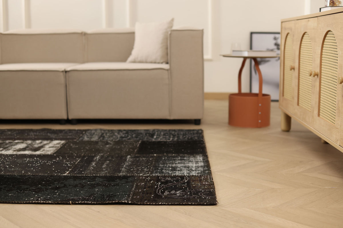 Vintage black patchwork Turkish area rug in wool and cotton with a distressed, overdyed bohemian design on a wooden floor.