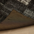 Handmade black patchwork Turkish area rug with distressed overdyed wool and cotton patterns on a wooden floor.