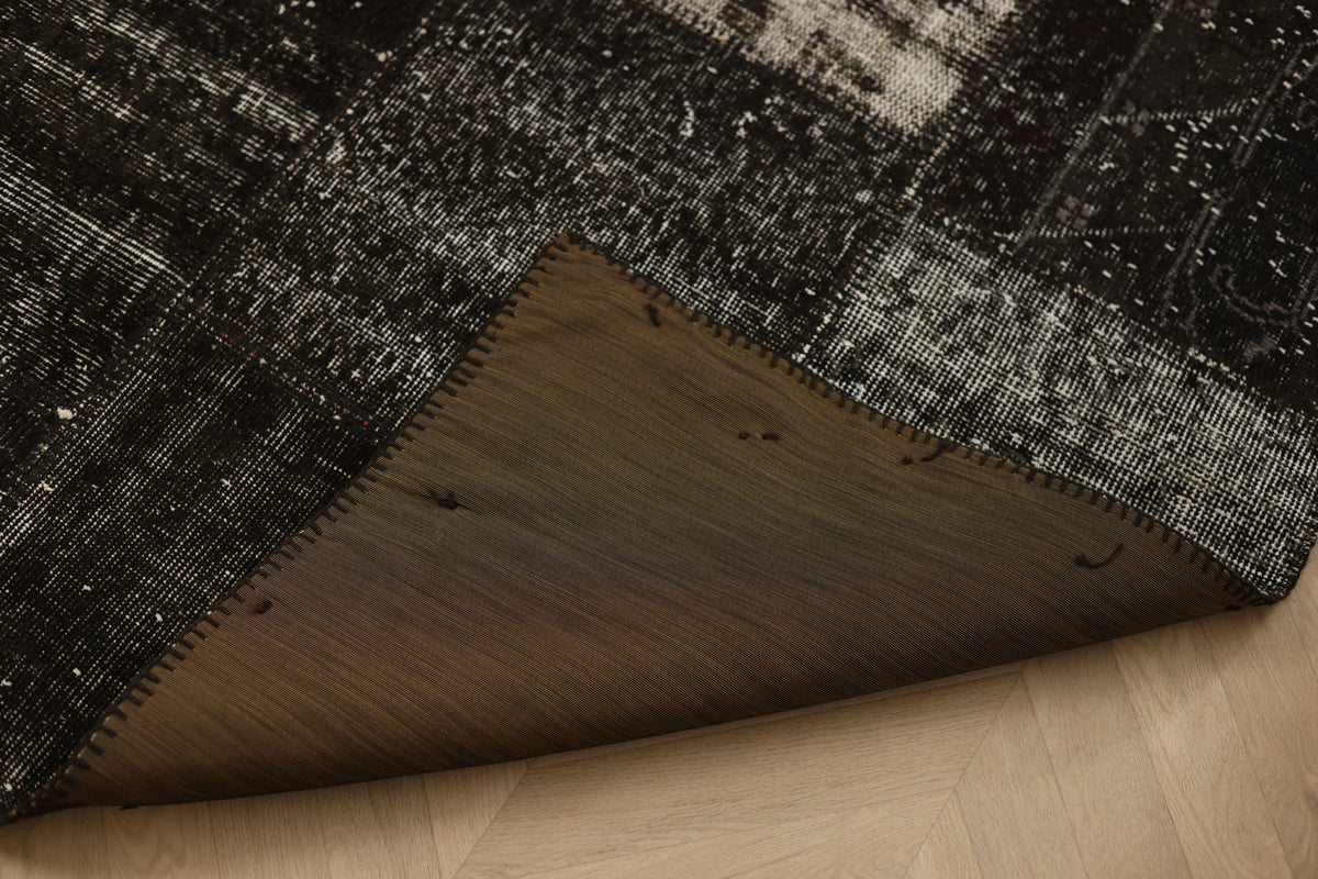 Handmade black patchwork Turkish area rug with distressed overdyed wool and cotton patterns on a wooden floor.