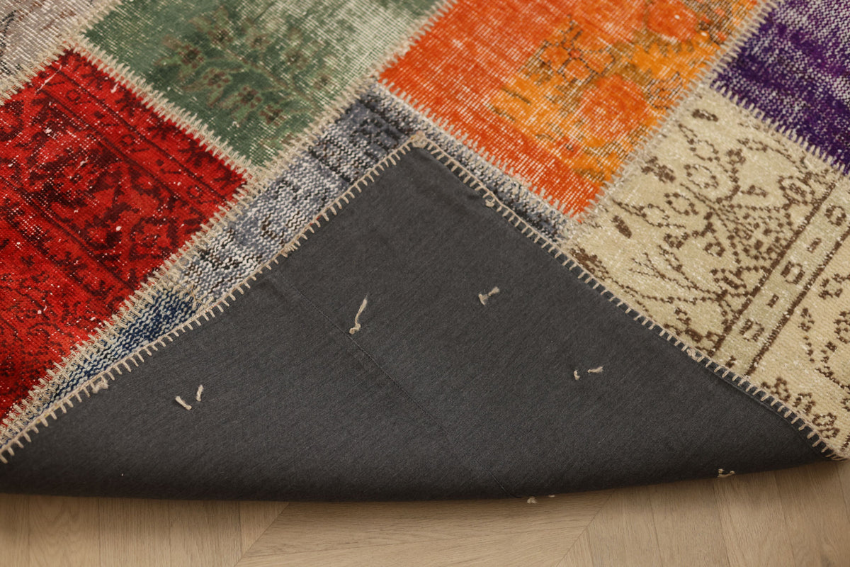 Handmade 5x7 ft vintage Turkish patchwork rug featuring vibrant floral wool and cotton squares with a dark fabric backing.