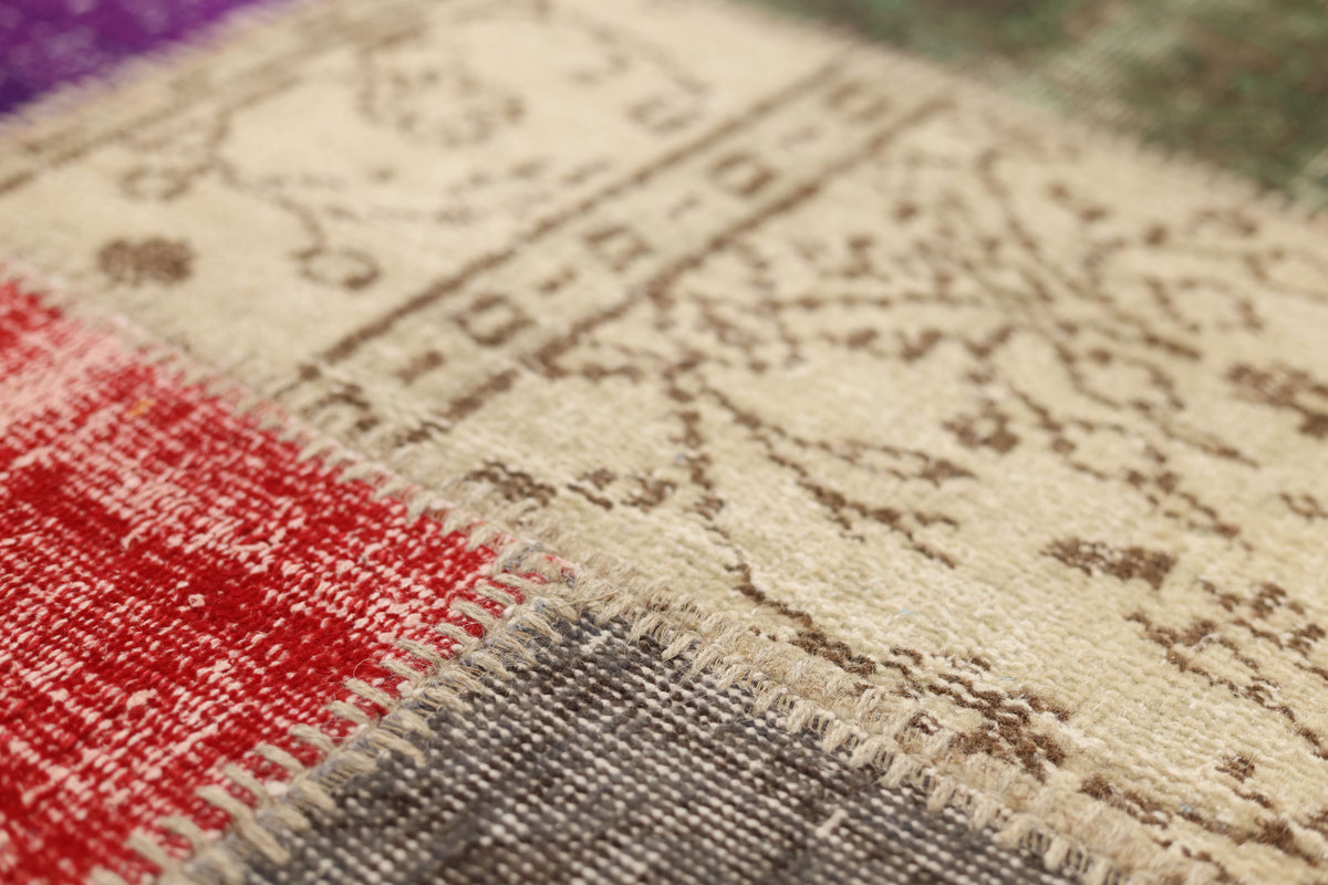 Handmade vintage Turkish patchwork rug featuring wool and cotton floral patterns in vibrant red, purple, and neutral tones.