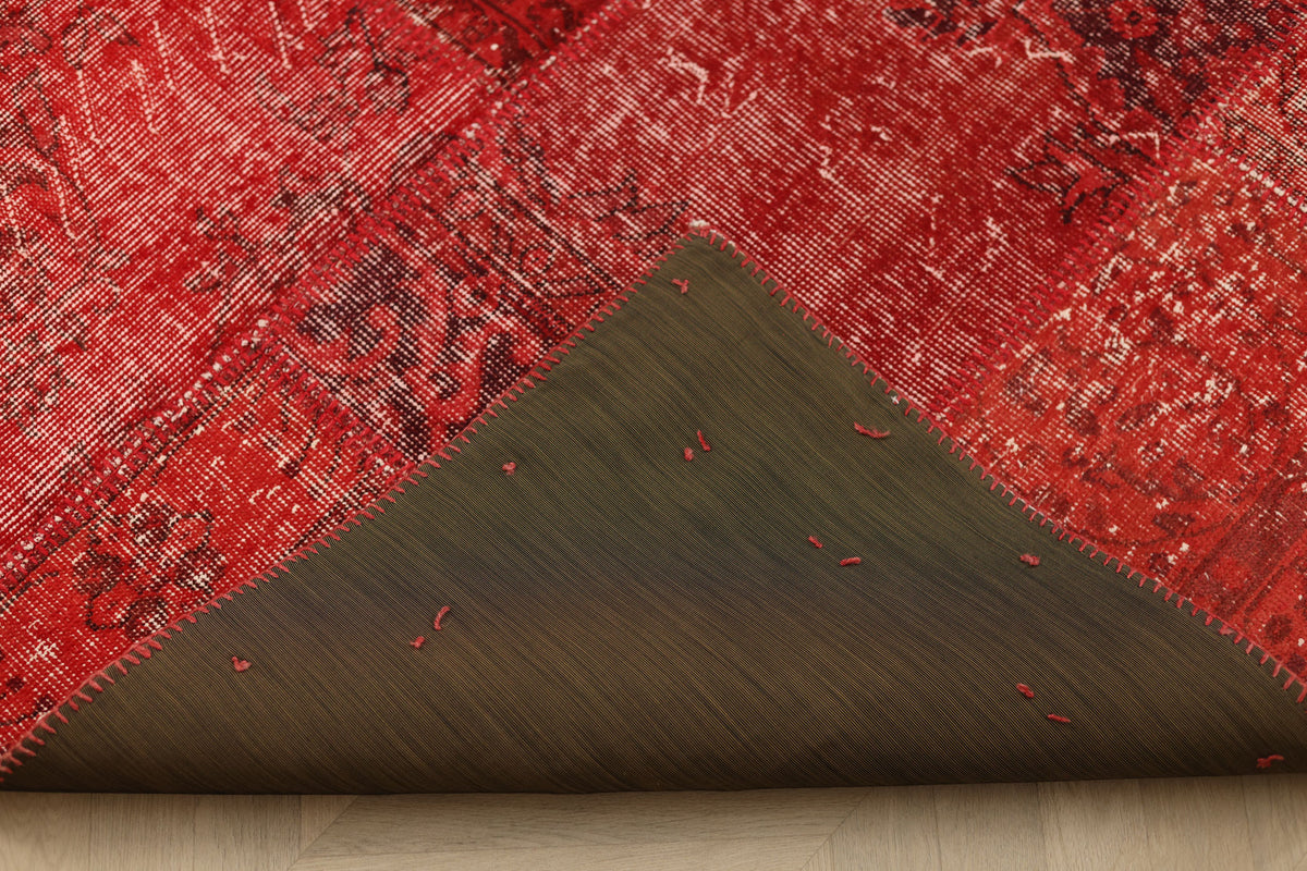 Handmade red patchwork Turkish area rug with a folded corner showing wool and cotton backing and stitched details.