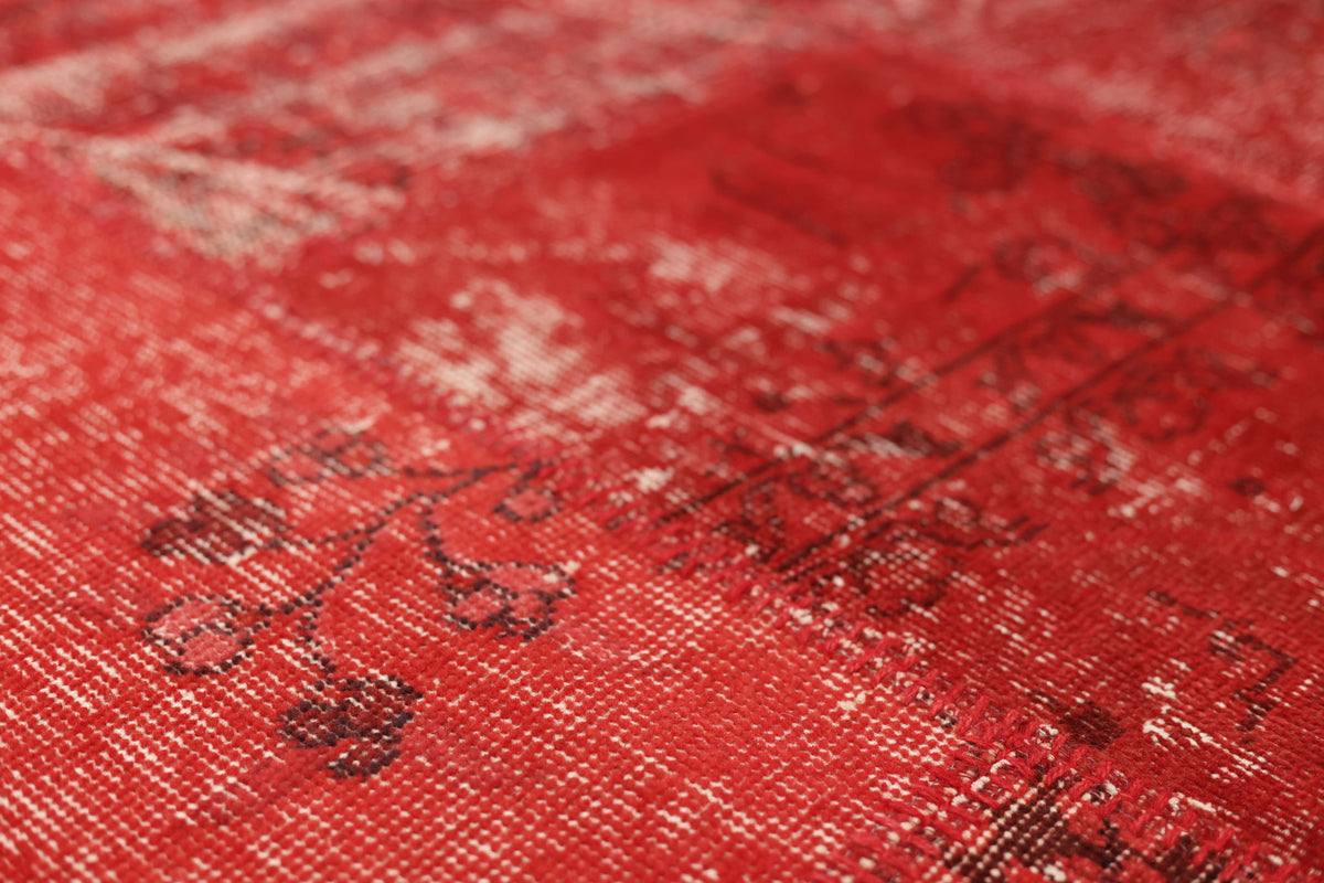 Close-up of a red vintage Turkish patchwork area rug featuring hand-stitched wool and cotton with faded bohemian patterns.