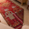 Handmade 3.3x11.5 ft wool and cotton Persian runner rug in red and orange with traditional human-figured patterns.