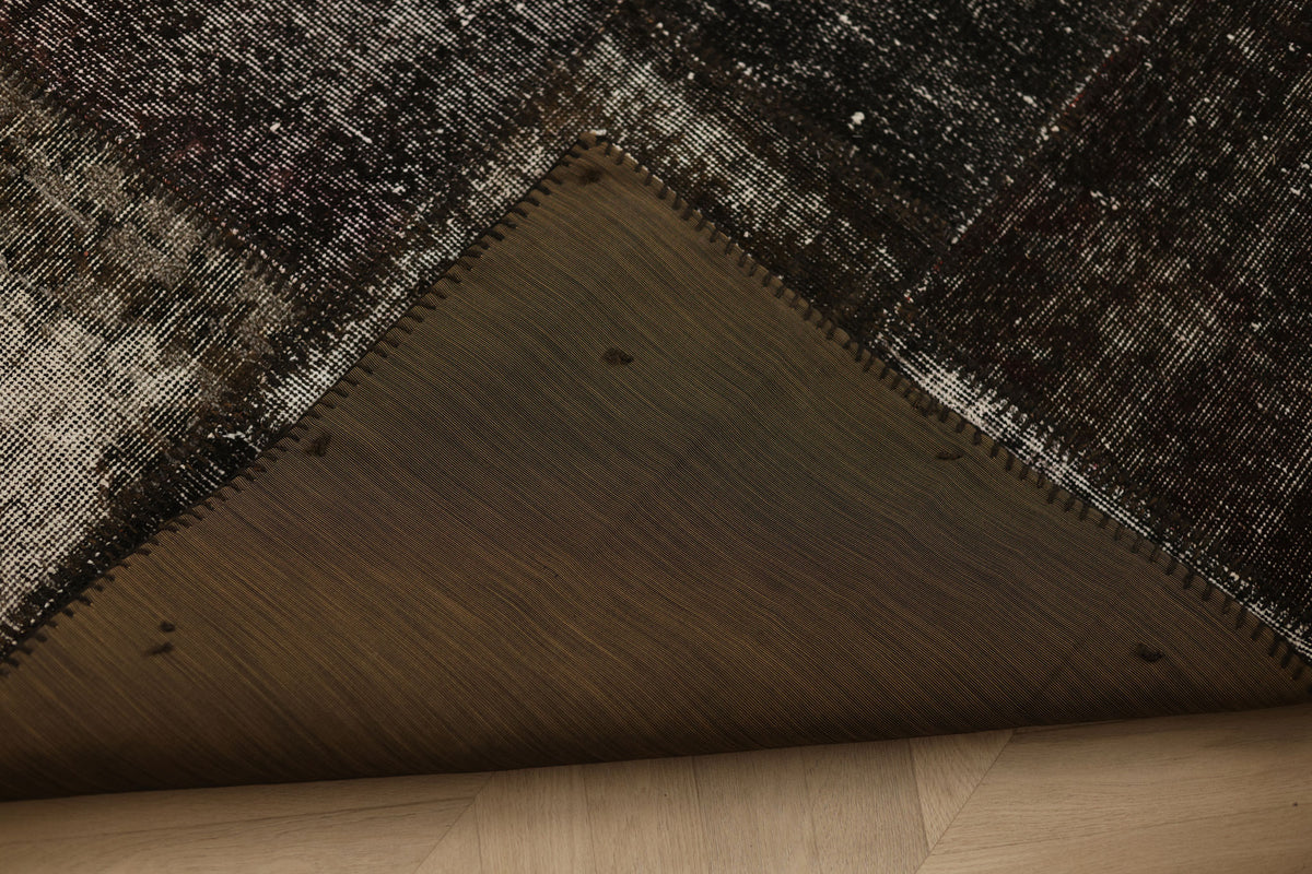 Handmade black patchwork Turkish area rug showing the stitched underside and distressed wool and cotton texture.
