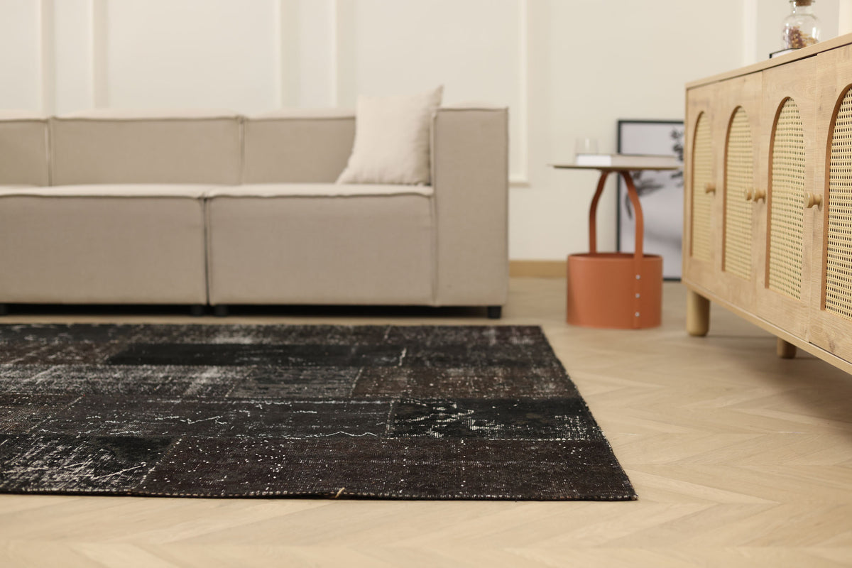 6x9 ft black patchwork vintage Turkish area rug with distressed wool and cotton patterns in a modern living room.