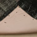 Back of a handmade black patchwork Turkish rug showing cotton backing and stitched seams on a 6x9 ft vintage wool piece.