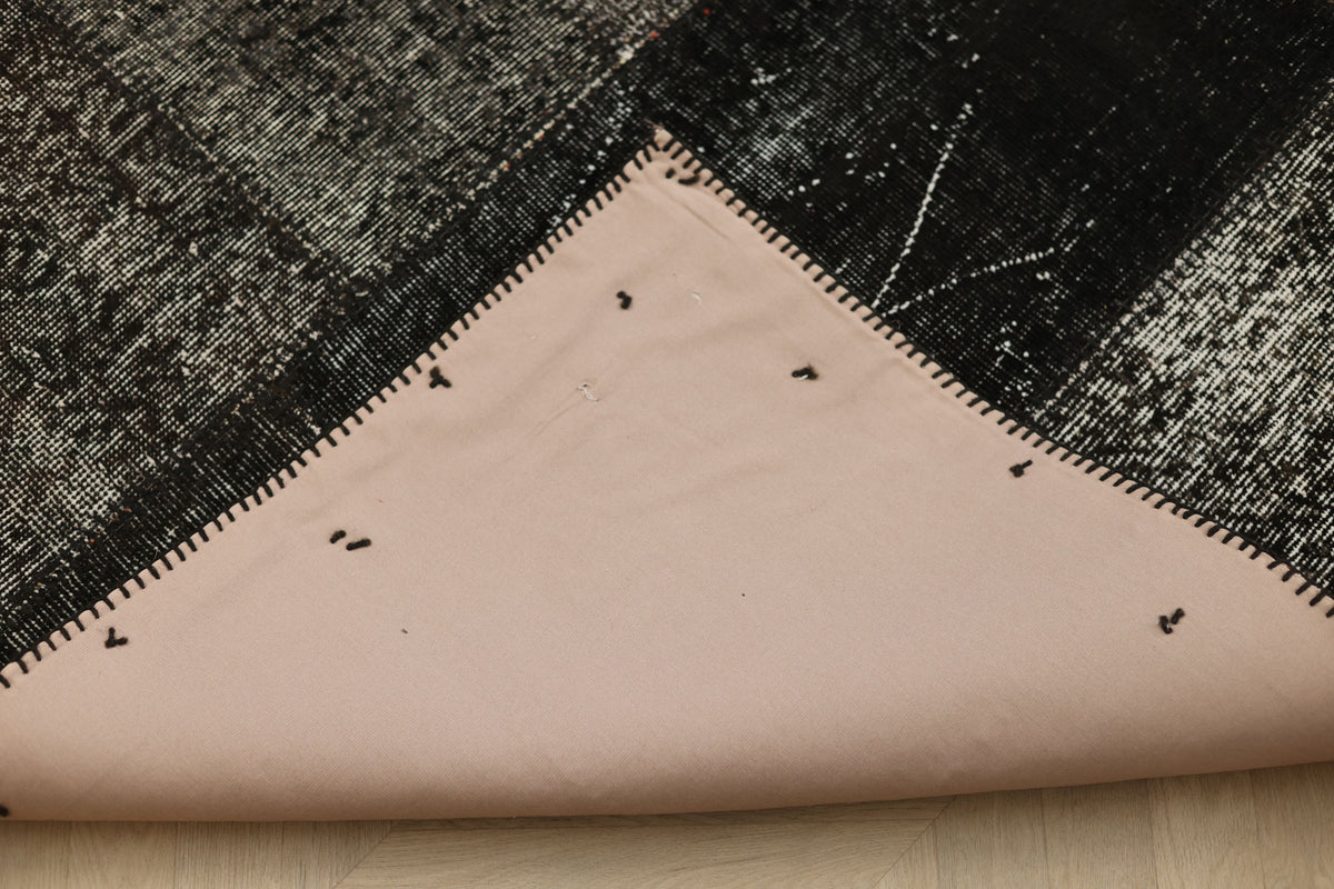 Back of a handmade black patchwork Turkish rug showing cotton backing and stitched seams on a 6x9 ft vintage wool piece.