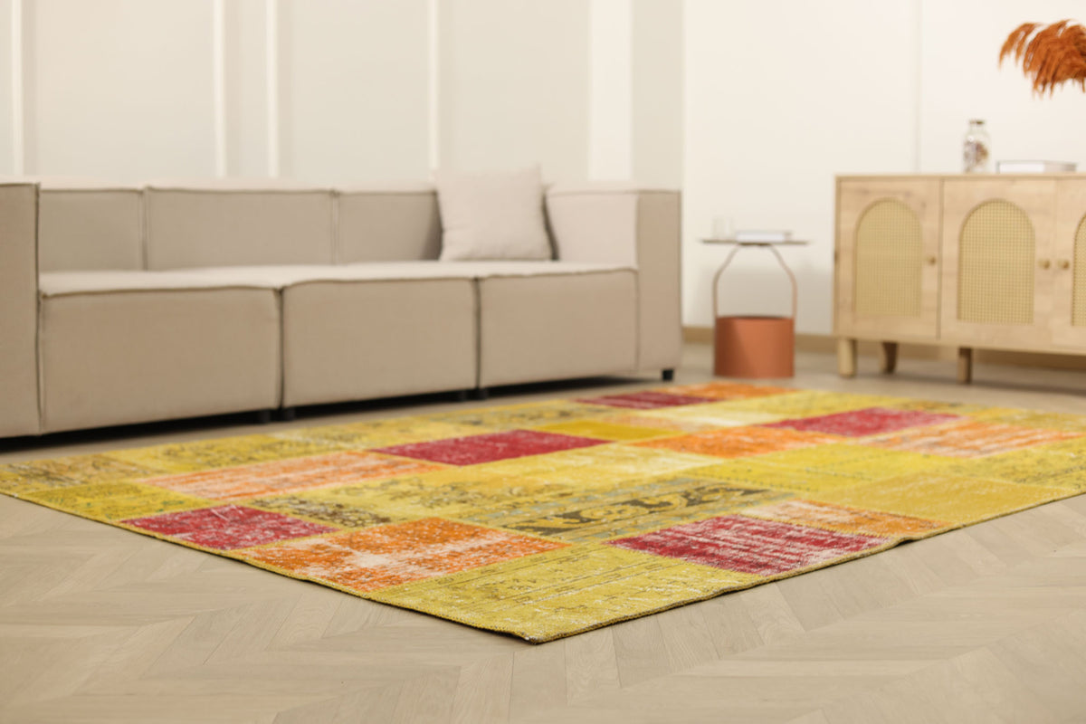6x9 ft vintage Turkish patchwork area rug in vibrant yellow and red with floral patterns on a hardwood floor.
