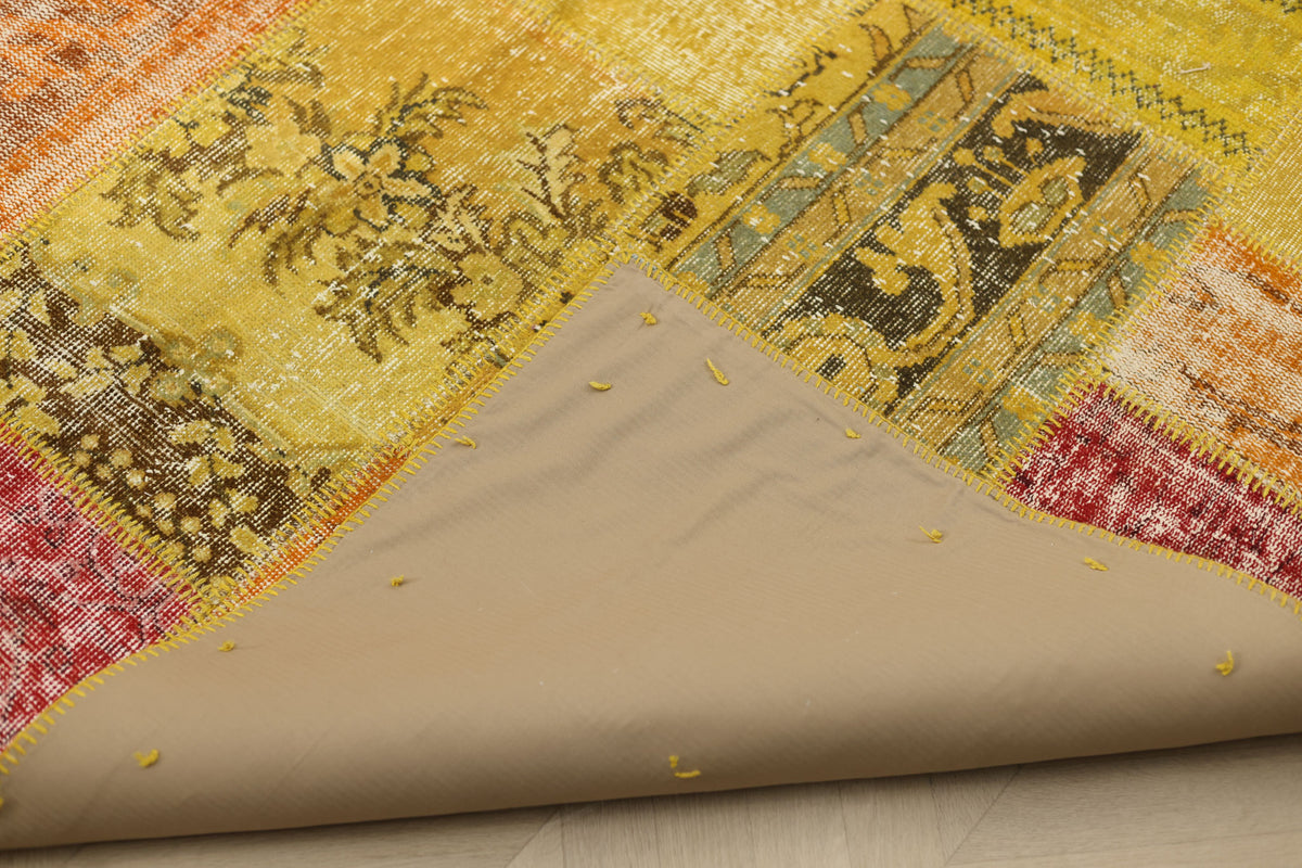 Handmade vintage Turkish patchwork rug in yellow and red with floral patterns, showing the cotton backing and stitching.