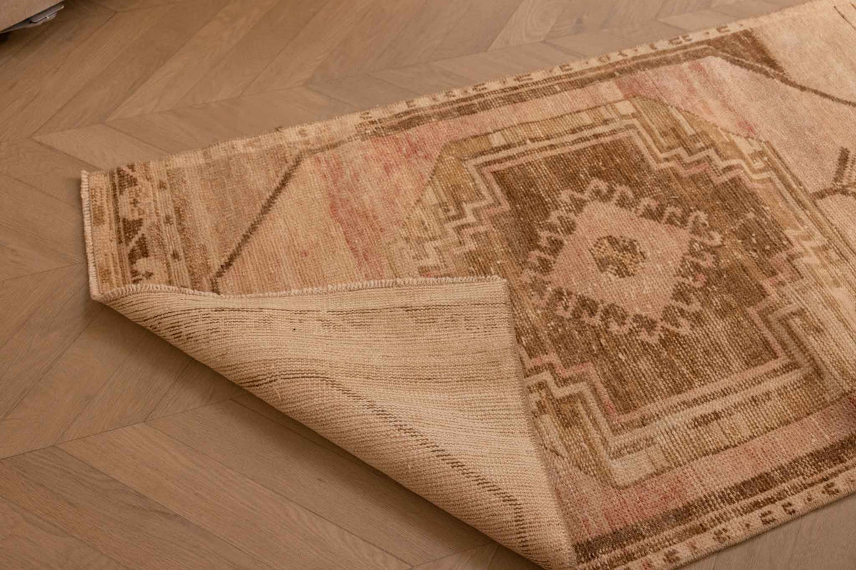 Hand-woven vintage Turkish runner rug in beige and red with geometric patterns, showing wool and cotton texture.