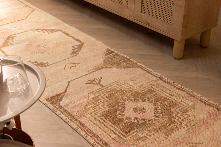 Hand-woven 2x11 ft vintage Turkish runner rug in beige and red with geometric patterns on a wooden floor.