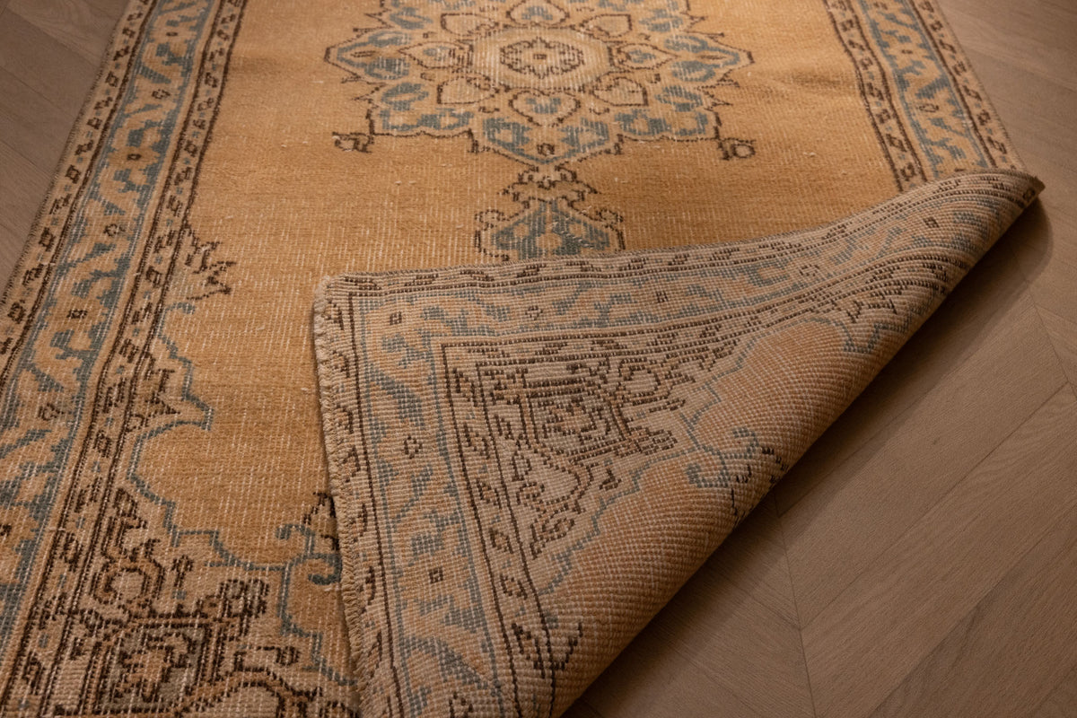 Handmade vintage Isparta runner rug in yellow and beige wool with traditional floral patterns and a folded corner.