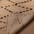 Handmade white and brown wool-cotton runner rug with geometric patterns and a folded corner showing its low-pile texture.