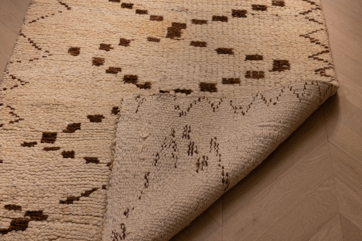 Handmade white and brown wool-cotton runner rug with geometric patterns and a folded corner showing its low-pile texture.