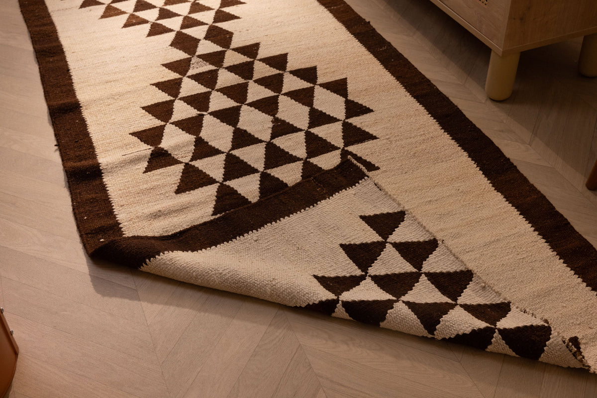 Handmade wool and cotton Persian-style runner rug in white and brown with geometric patterns on a wooden floor.