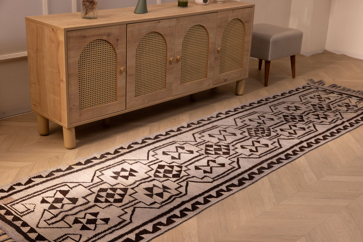 Handmade 3x11 ft gray and brown wool-cotton Persian kilim runner with geometric patterns on a wooden floor.