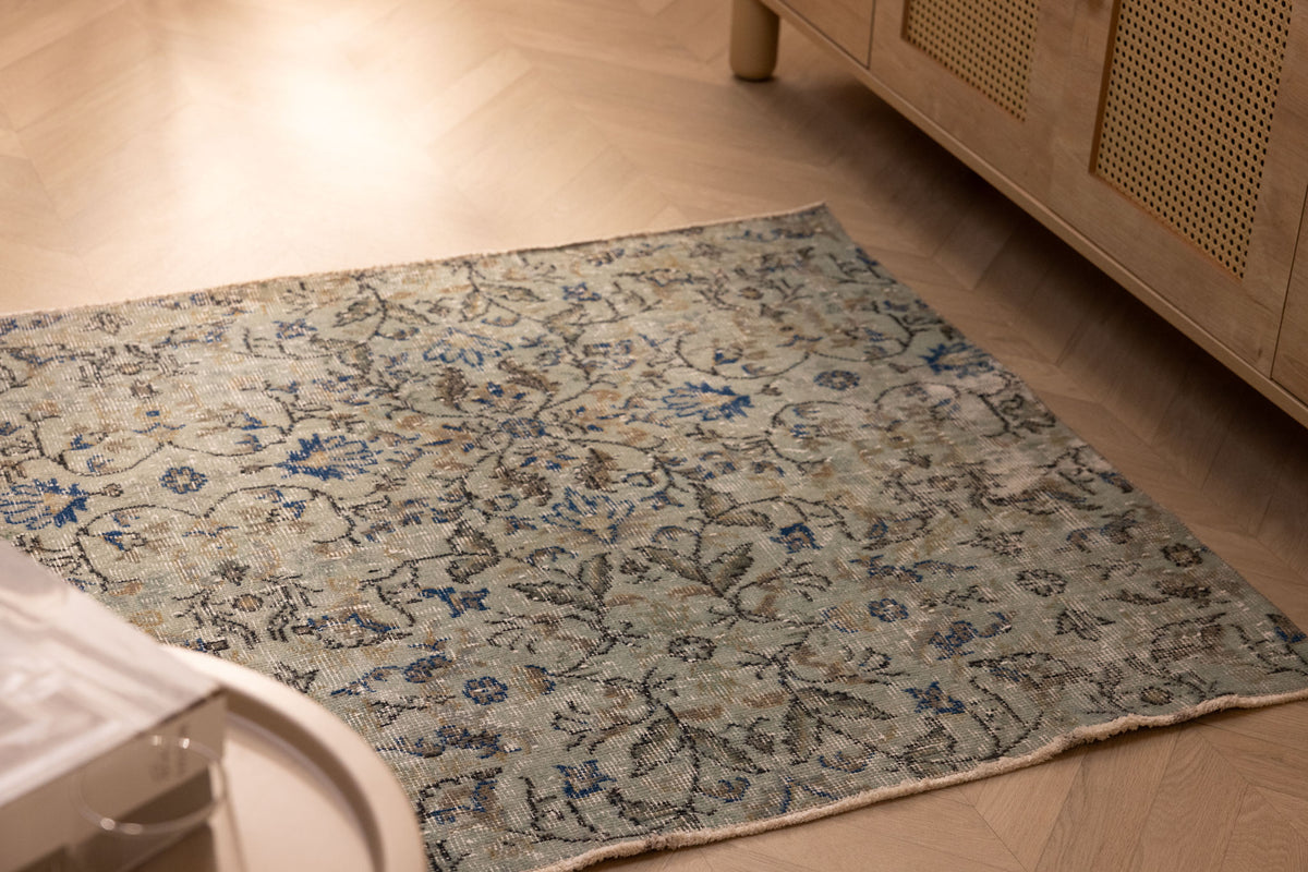 Hand-woven vintage Isparta wool and cotton doormat in gray and navy floral patterns on a wooden floor.