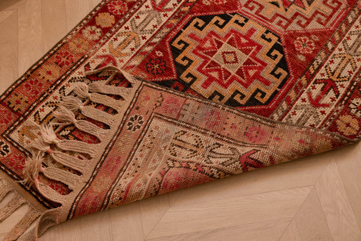 Handmade wool and cotton Persian-style runner rug in red and brown with geometric floral patterns and tasseled edges.