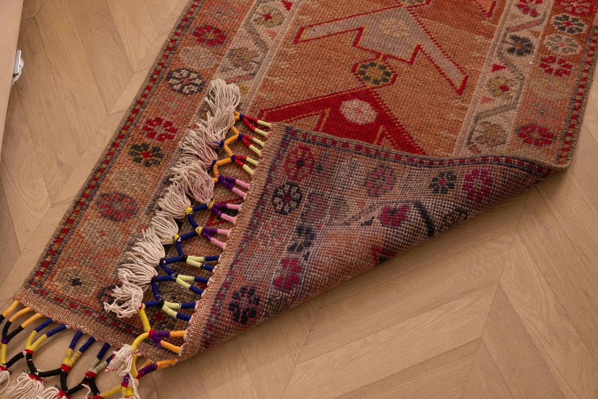 Handmade wool and cotton Persian-style runner in brown and beige with geometric floral patterns and colorful tasseled fringe.