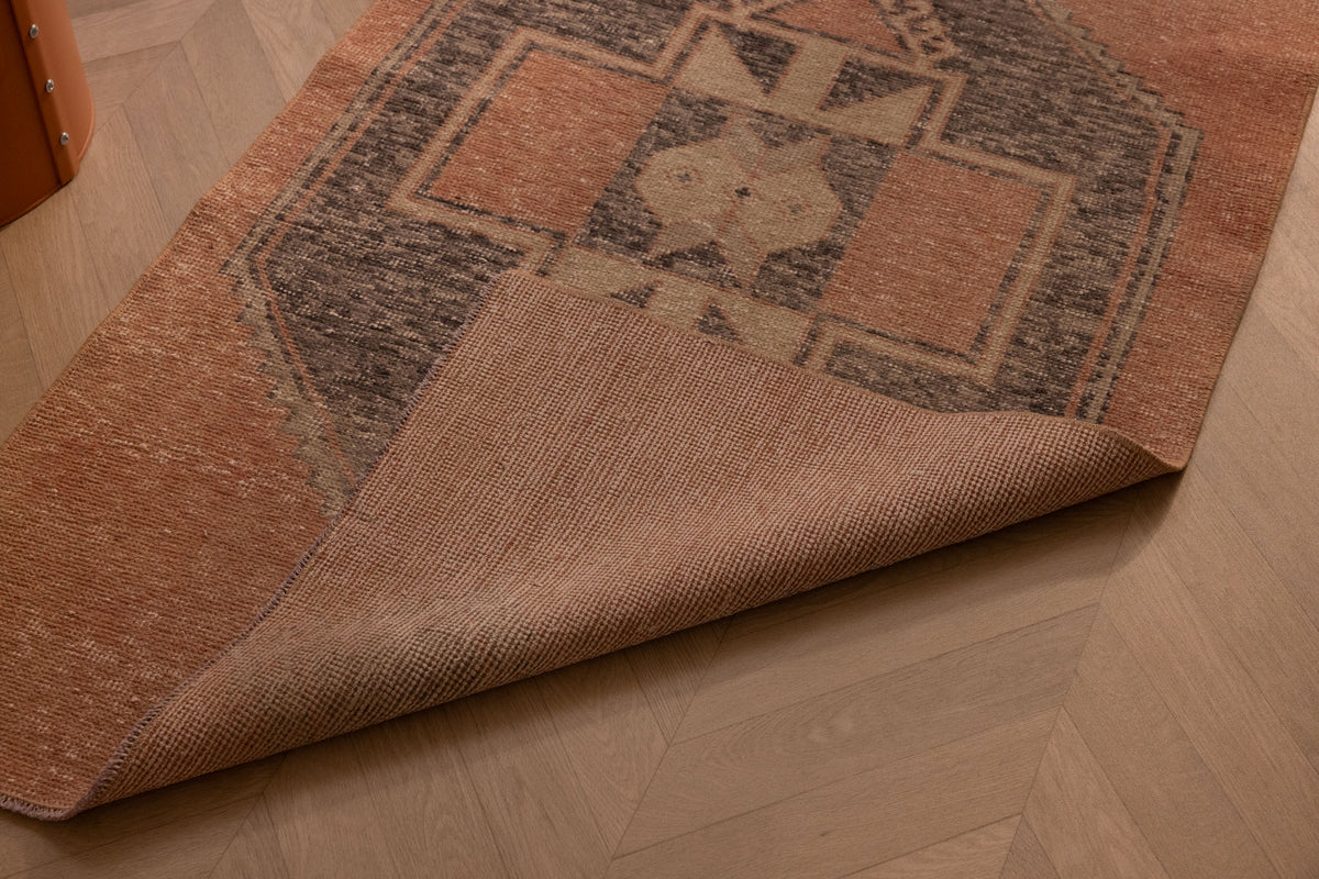 Hand-woven vintage Turkish runner rug in burnt orange and gray with geometric patterns on a wooden floor.