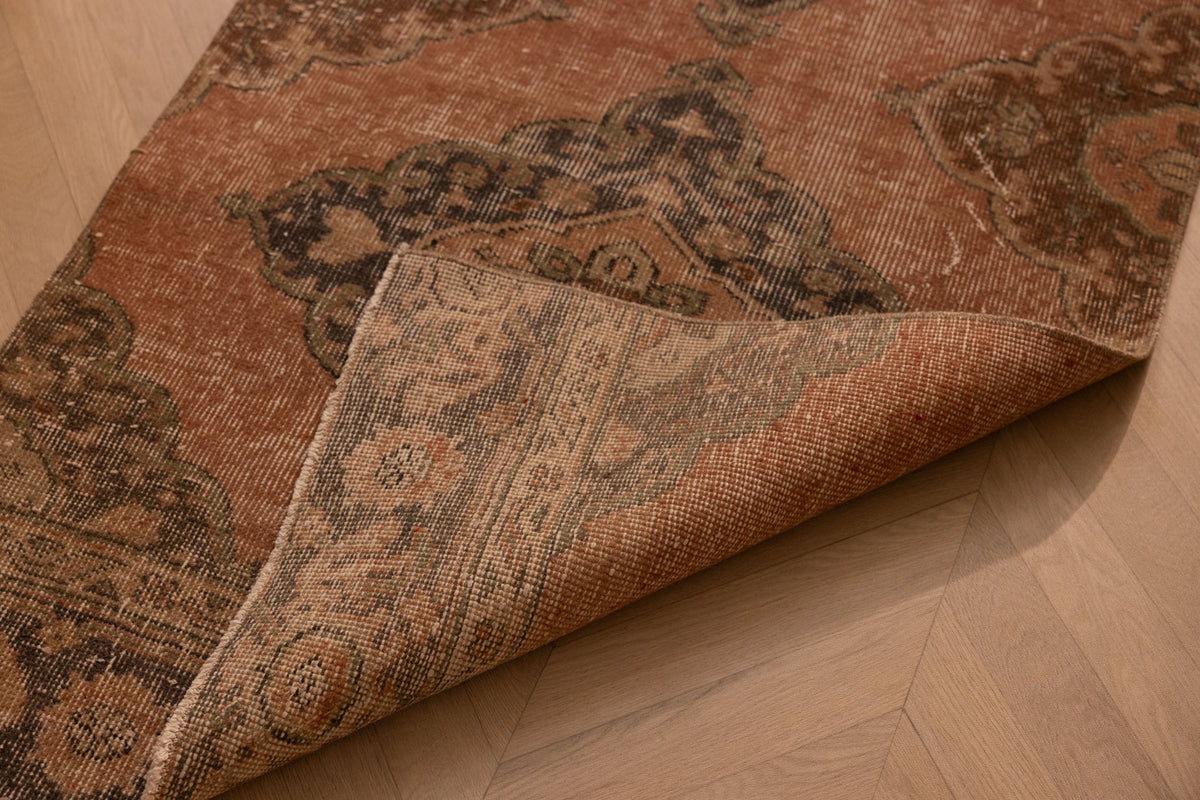 Vintage burnt-orange Konya runner rug with floral motifs, hand-woven in wool and cotton with a folded corner detail.