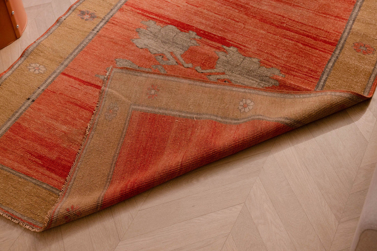 Hand-woven vintage Sivas wool runner rug in burnt orange and brown with floral motifs and a folded corner.