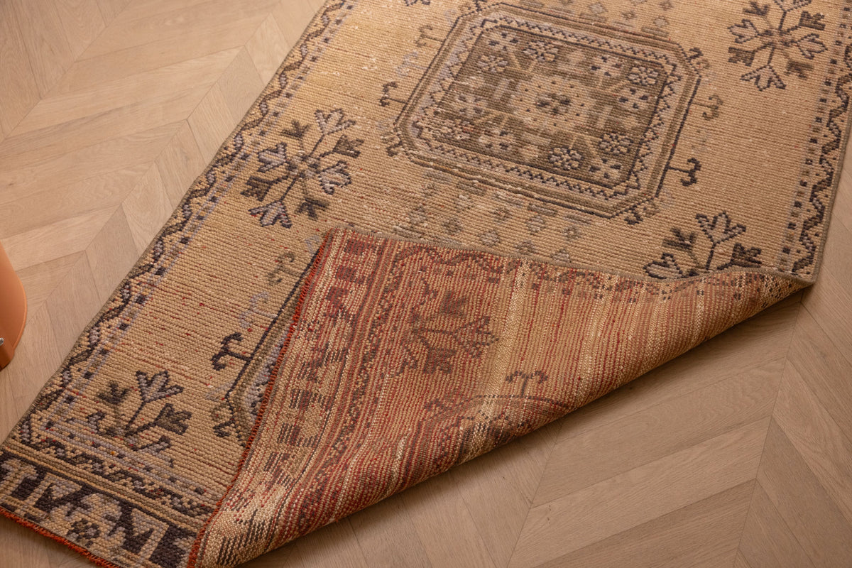 Vintage beige Konya runner rug with geometric patterns, hand-woven from wool and cotton, shown with a folded corner.
