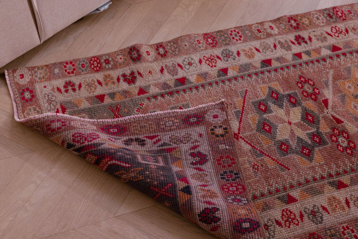 Handmade beige wool and cotton Persian-style runner rug with floral, maximalist patterns and a folded corner.