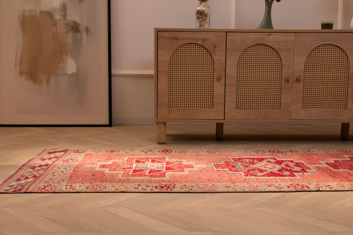 Handmade pink Persian-style wool and cotton runner rug with geometric patterns on a wooden floor.